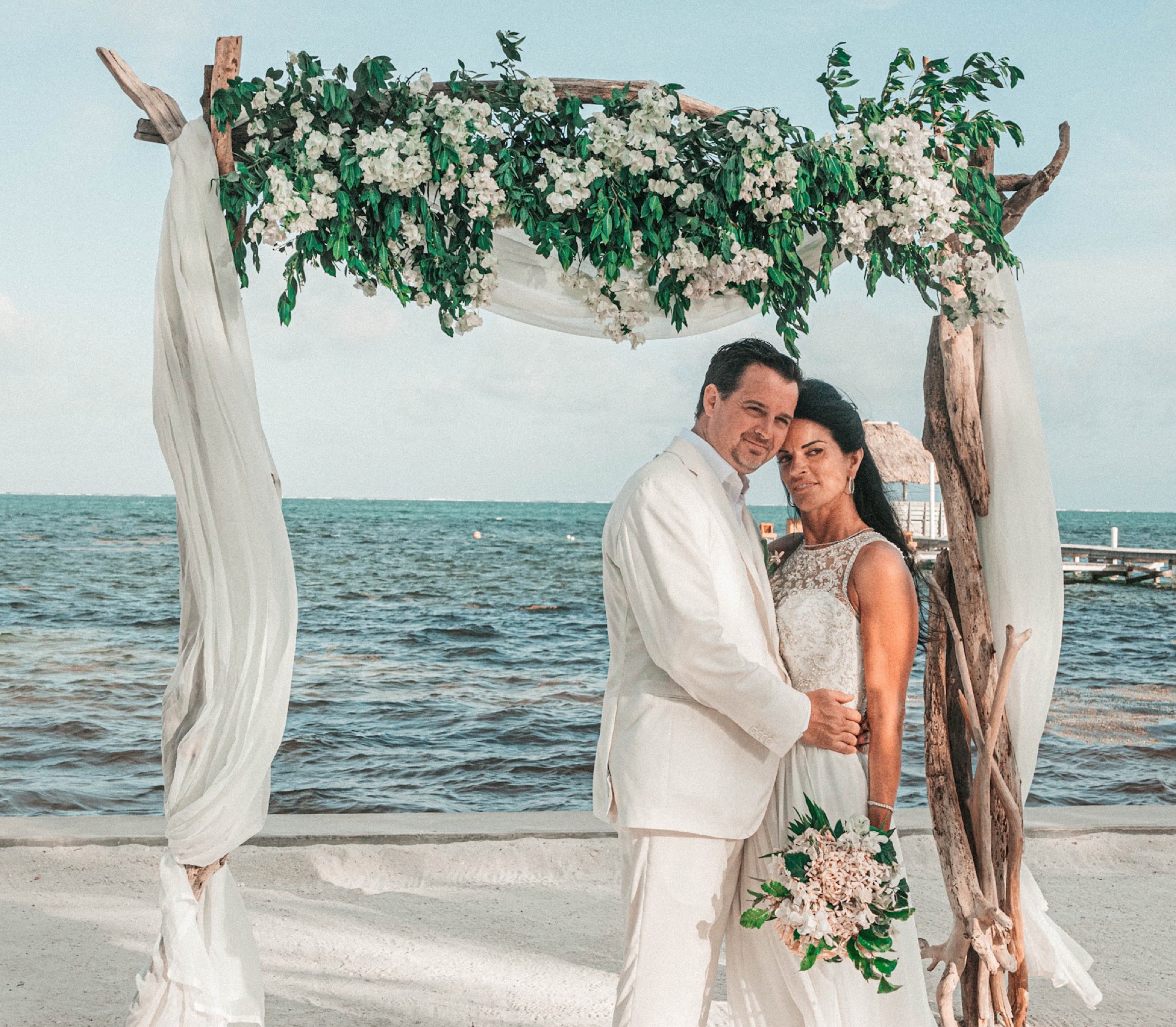 Bride and groom under a flower arch on a Belize beach